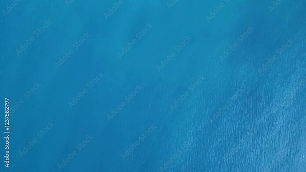 This footage was taken by using a drone flying above a blue ocean with smooth waves.