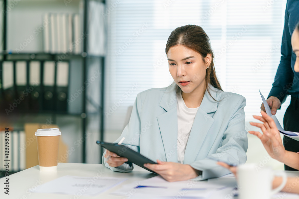 A professional woman reviews documents on a tablet in a modern office setting, collaborating with colleagues. A professional woman reviews documents on a tablet in a modern office setting, collaborating with colleagues.