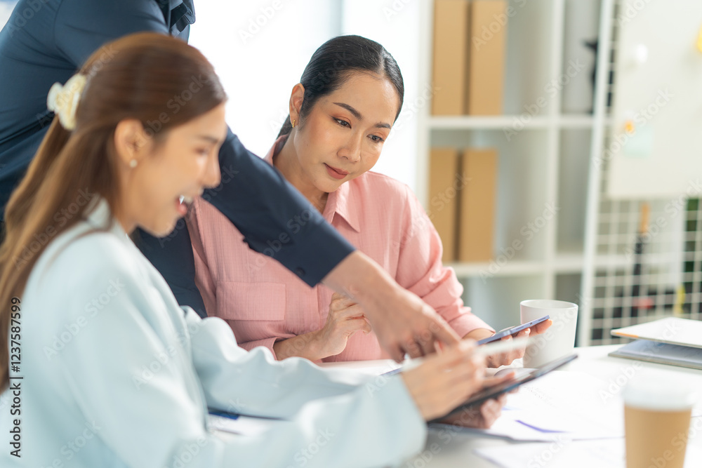 Two women collaborate at a table, discussing ideas while a man points at a tablet. The setting is bright and modern, emphasizing teamwork. Two women collaborate at a table, discussing ideas while a man points at a tablet. The setting is bright and modern, emphasizing teamwork.