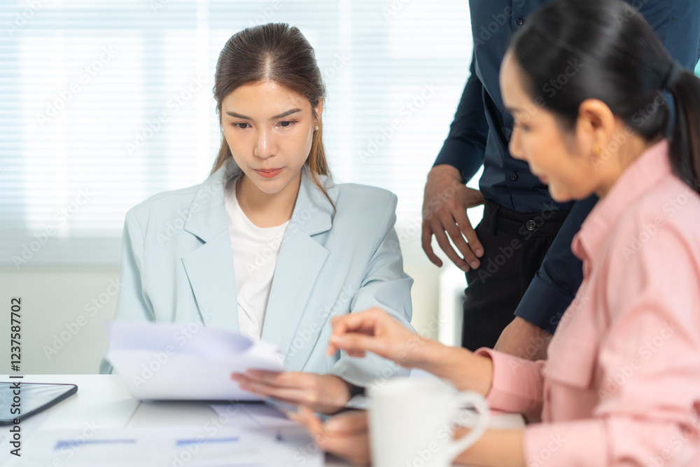 Obraz premium Two women collaborate at a table, reviewing documents, while a man stands nearby, suggesting teamwork and business discussions.