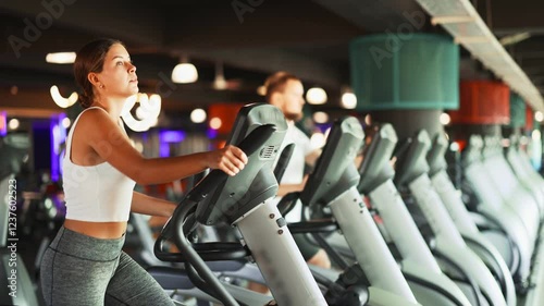 Young athletic woman in sportswear training on elliptical machine in gym