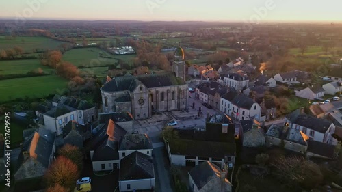 Eglise Saint-Gervais et Saint-Protais, church, Jublains town at sunset, Mayenne in France. Aerial drone backward tilt-up reveal photo