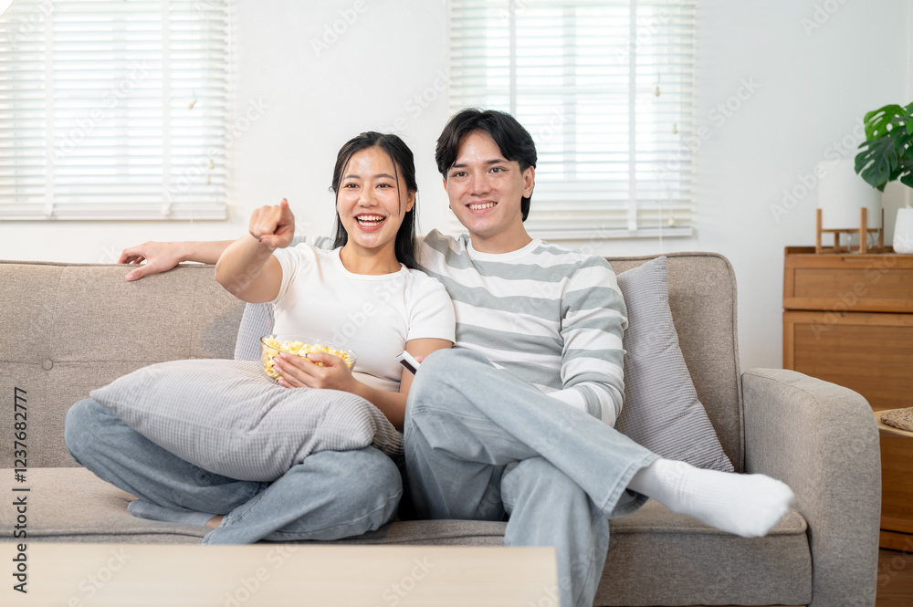 Cheerful Asian boyfriend and girlfriend enjoy watching a movie on the TV while sitting on the sofa. Cheerful Asian boyfriend and girlfriend enjoy watching a movie on the TV while sitting on the sofa.
