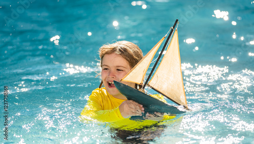 Little boy playing with toy sailing boat, toy ship. Travel and adventure concept. Child feeling adventurous while cruising. Kid on summer sunset beach. Kid playing on the beach at the sunset time.