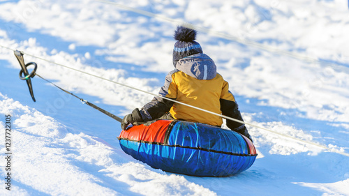 A little boy-child rides a tubing down a hill in the snow in winter. Child on a ski lift and snow-capped mountains. Winter entertainment. Snow fun...