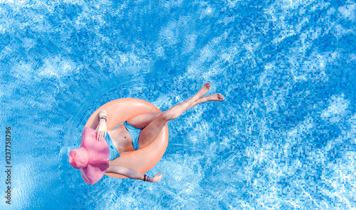 Beautiful woman in hat relaxes in swimming pool aerial drone view from above, young girl in bikini swims on inflatable ring donut and has fun in water on tropical vacation on holiday resort
