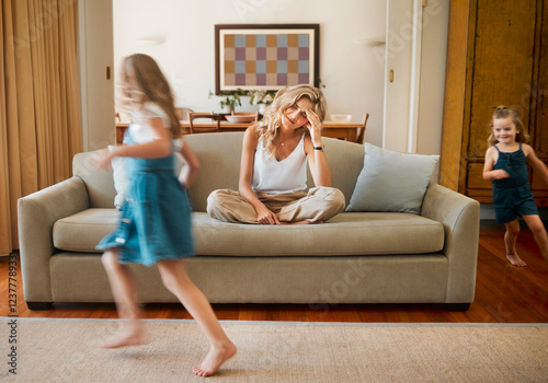 ADHD, motion blur and stress of mother with children running in living room of home for hyperactivity. Anxiety, autism and energy with unhappy woman parent on sofa in apartment for break or rest