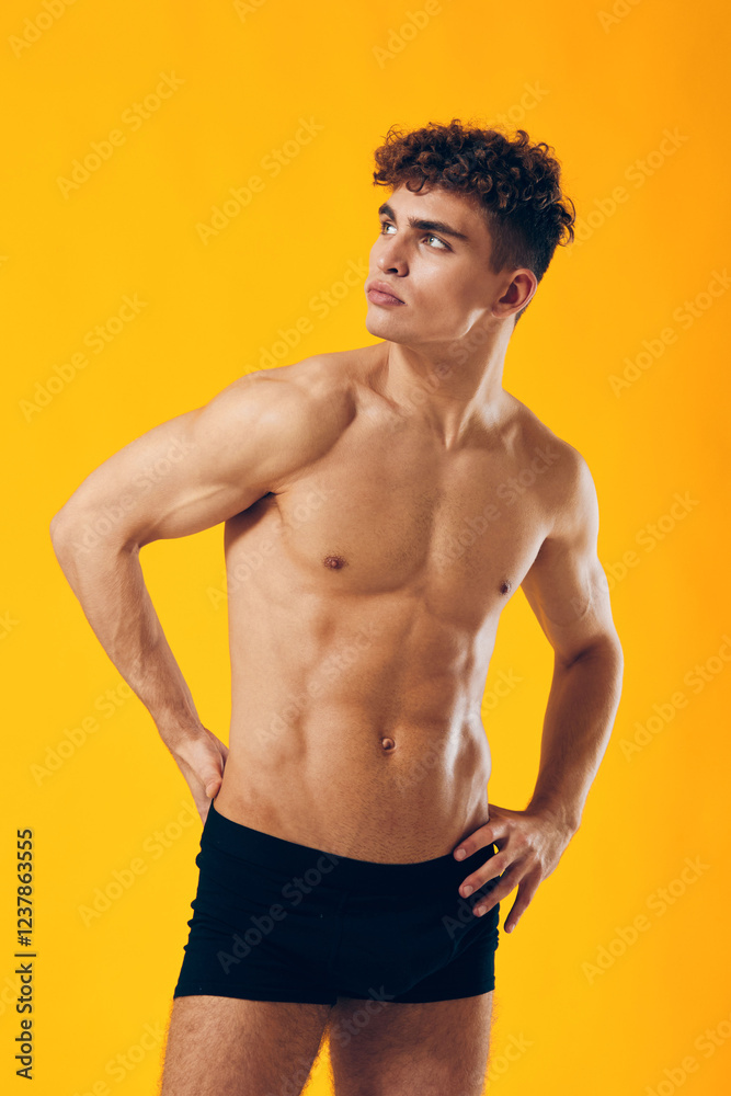 Fototapeta premium Confident young man posing in black underwear against a vibrant yellow background, showcasing fitness and healthy lifestyle. Body positivity and self-expression concept.