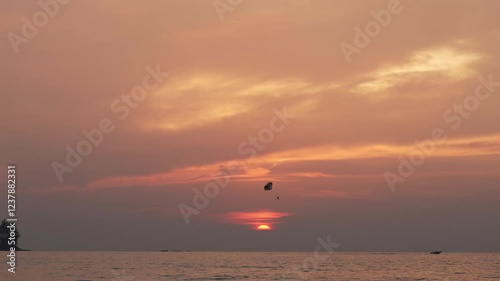 Parasailing experience at dusk showcases the beauty of the sunset over the ocean. Spectators watch as the parasailer glides through the vibrant sky. photo