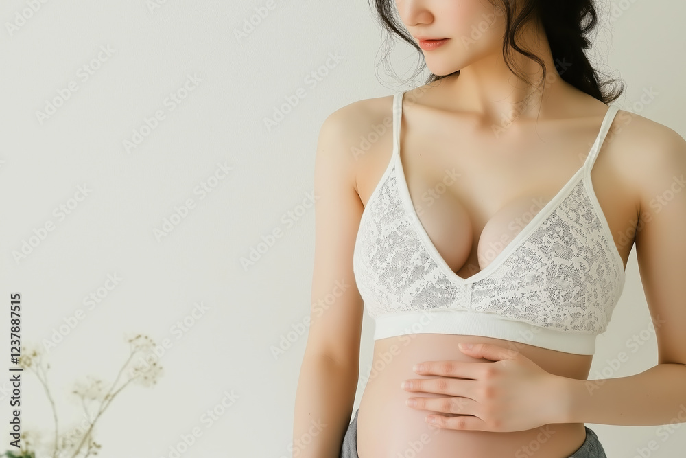 Obraz premium Pregnant Asian Woman in Lace Bra Holding Belly in Minimalist Setting