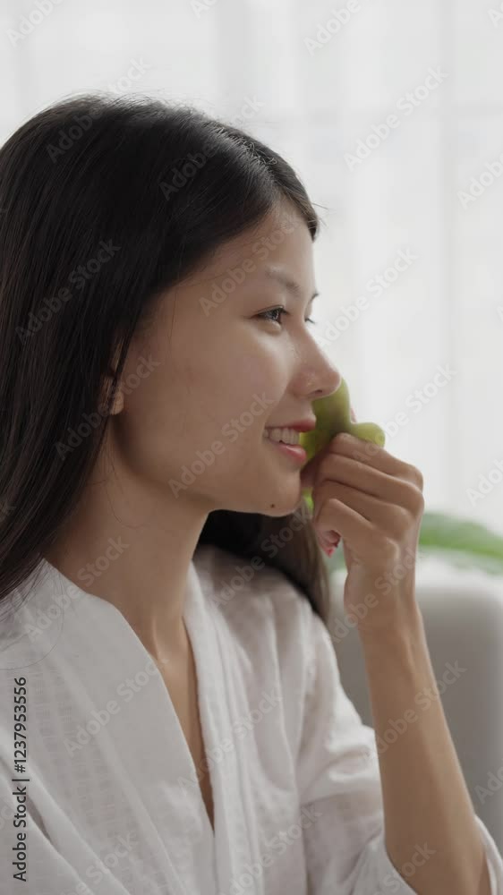 Asian woman in bathrobeses gua sha quarz lifting tool on face. Woman self massage with jade gouache scraper Asian woman in bathrobeses gua sha quarz lifting tool on face. Woman self massage with jade gouache scraper