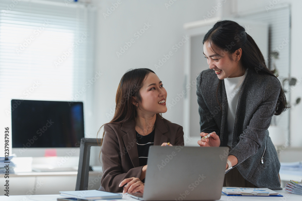 Two happy asian businesswomen collaborating on a project while discussing ideas and strategies, working together on a laptop in a bright, modern office environment Two happy asian businesswomen collaborating on a project while discussing ideas and strategies, working together on a laptop in a bright, modern office environment