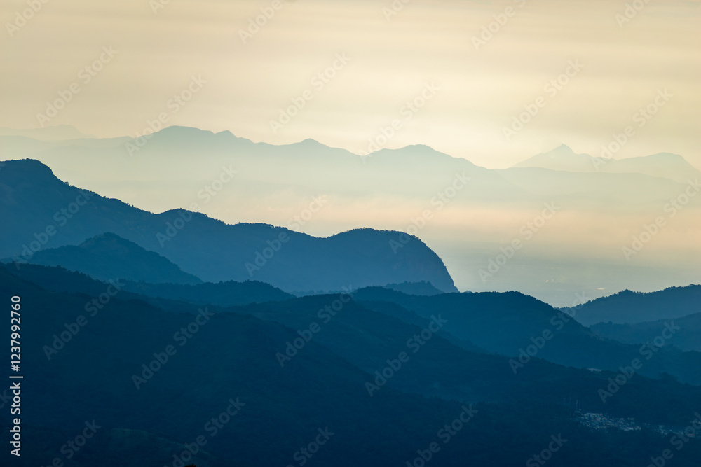 Obraz premium Soft sunlight breaks over the misty hills of Kodaikanal, highlighting the layered mountain ranges.