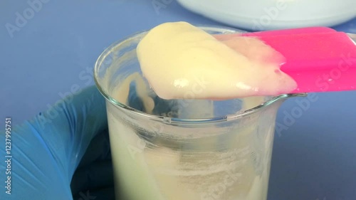 Macro shot of a cosmetic emulsion being prepared in a laboratory. The video captures the operator's gloved hands mixing ingredients in a beaker, showcasing the precision and technique involved in cosm