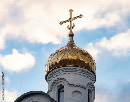 Golden dome of church with cross against background of sky with clouds.