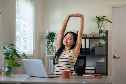 A carefree Asian businesswoman is stretching her arms to relax after finishing her work on a laptop.
