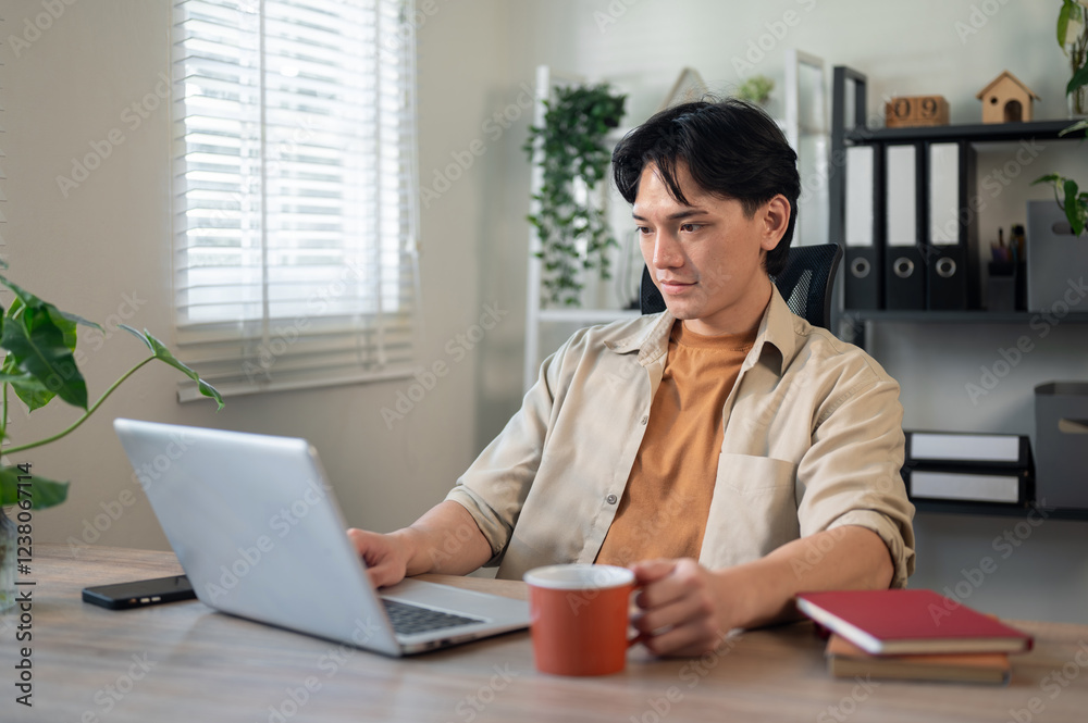 A handsome, smart Asian businessman is working on his laptop at a desk in his minimalist office. A handsome, smart Asian businessman is working on his laptop at a desk in his minimalist office.