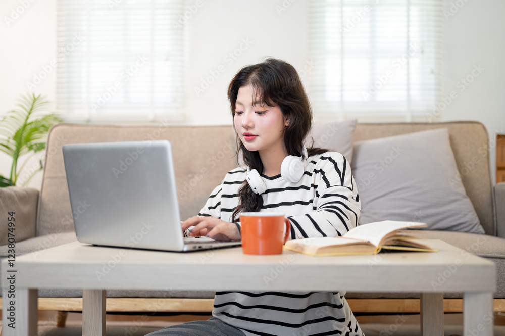 A beautiful Asian female college student sits at a coffee table, studying online through her laptop. A beautiful Asian female college student sits at a coffee table, studying online through her laptop.