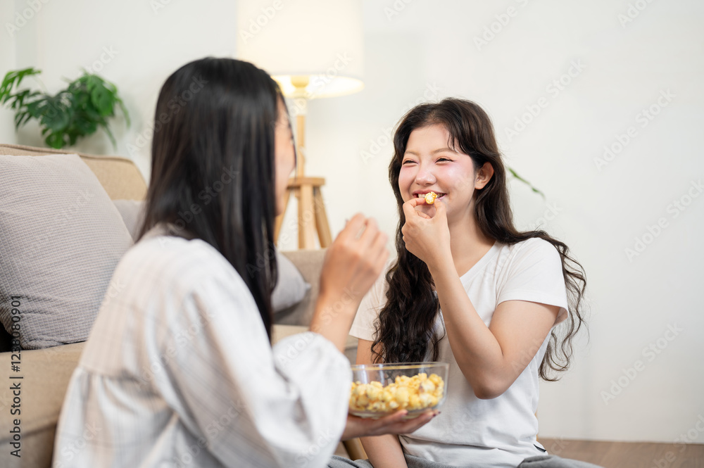 Two happy young Asian women are enjoying popcorn and a conversation together in the living room. Two happy young Asian women are enjoying popcorn and a conversation together in the living room.