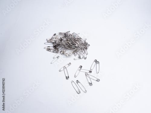 metallic safety pins attached to a larger safety pin, displayed against a white background.. A pile of shiny stainless steel safety pins on a white background.
