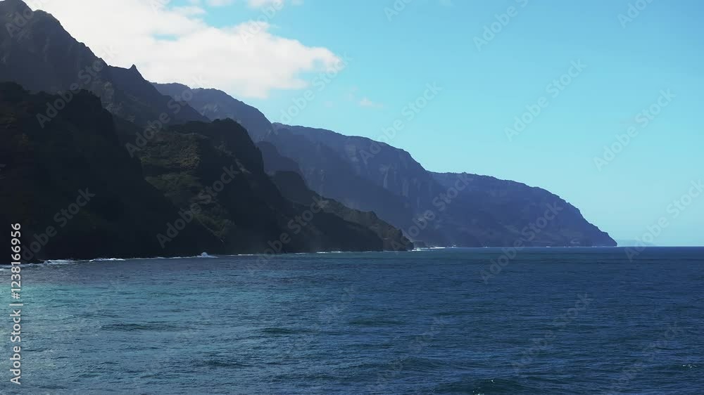 Aerial view of the Napali Coast on Kauai Island, Hawaii, with jagged cliffs, lush greenery, turquoise waters, and gentle ocean waves in motion. Aerial view of the Napali Coast on Kauai Island, Hawaii, with jagged cliffs, lush greenery, turquoise waters, and gentle ocean waves in motion.