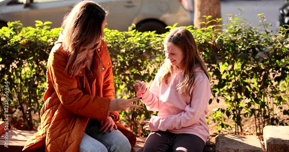 Loving mother and daughter play rock paper scissors game sitting on bench in park. Woman with girl enjoys funny activity spending time slow motion