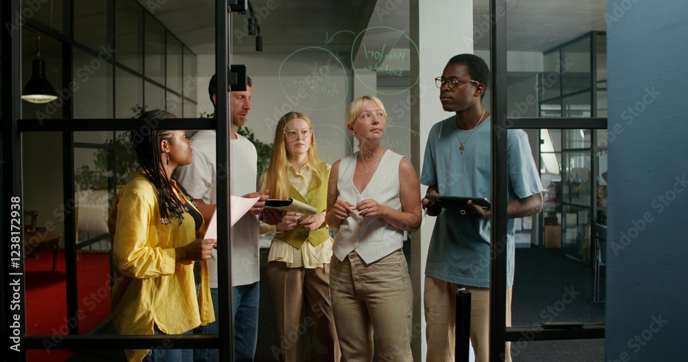 Obraz premium A group of young people of different nationalities are talking standing near a glass board with notes. Business planning. Daylight
