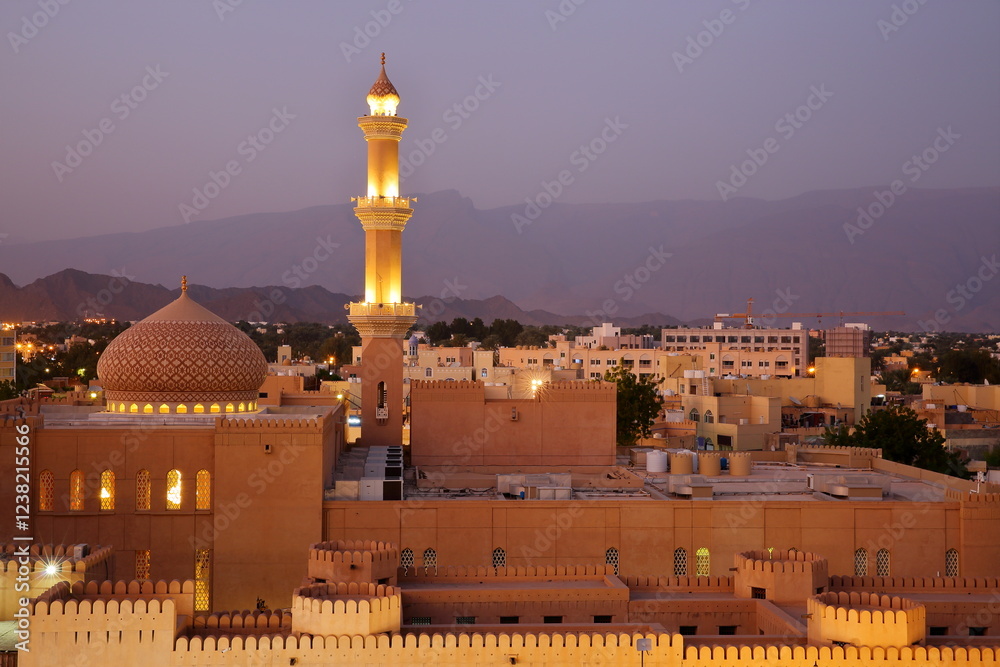 General night view of the town of Nizwa, Al Dakhiliyah, Oman, with the mosque, its minaret and the ramparts of Nizwa fort in the foreground. Picture taken during the blue hour