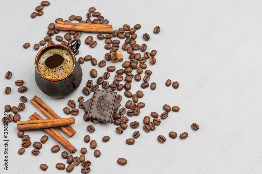 Coffee drink in black cup. Cinnamon sticks, pieces of chocolate and coffee grains on table