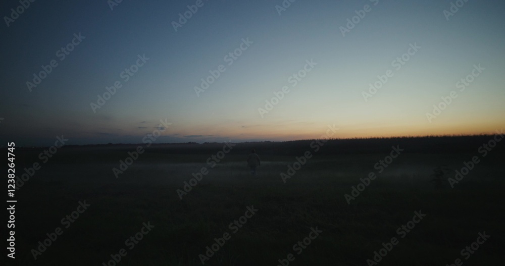 A man runs across a field on a summer evening after sunset. Rear view, unrecognizable person. A man runs across a field on a summer evening after sunset. Rear view, unrecognizable person.