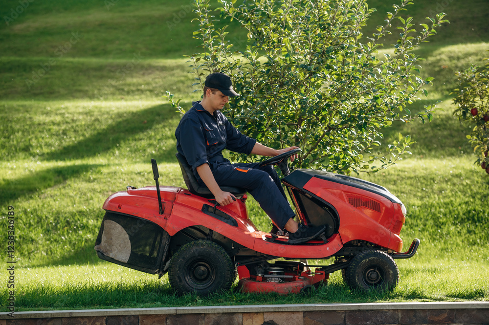 Red colored lawn mover, sitting on it. Professional gardener is on the lawn Red colored lawn mover, sitting on it. Professional gardener is on the lawn