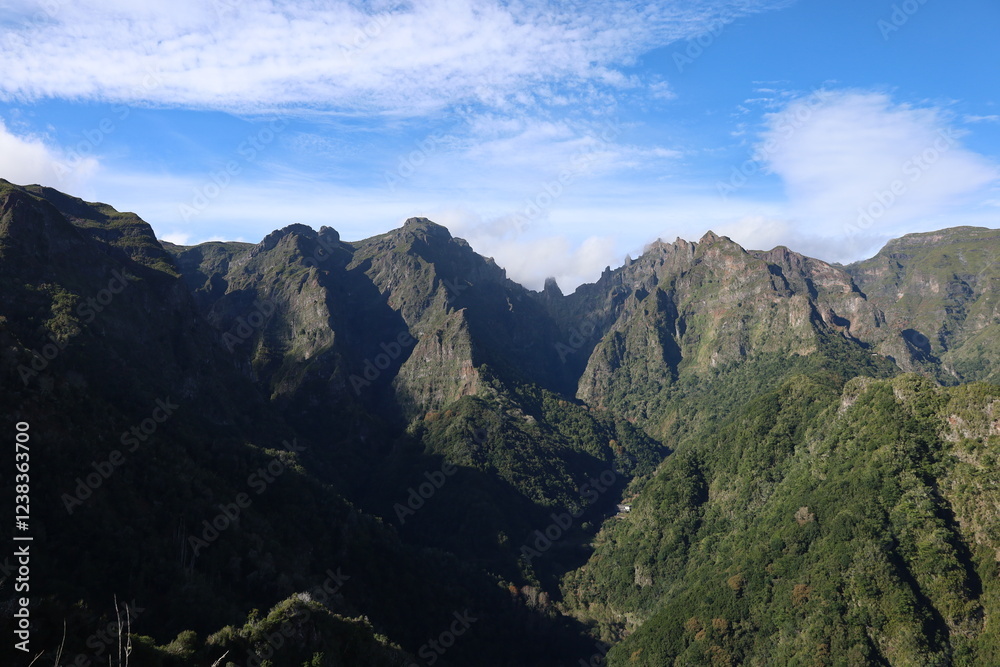 Towering mountains rise sharply against a brilliant blue sky, surrounded by dense green forests. Sunlight casts shadows, highlighting the rugged terrain and natural splendor. Towering mountains rise sharply against a brilliant blue sky, surrounded by dense green forests. Sunlight casts shadows, highlighting the rugged terrain and natural splendor.