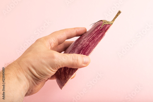 Hand holding sliced Purple eggplant with white stripes on pink pastel, Side view, copy space. photo