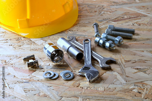 Yellow helmet, bolts, nuts, wrenches, maintenance concept, on wooden background