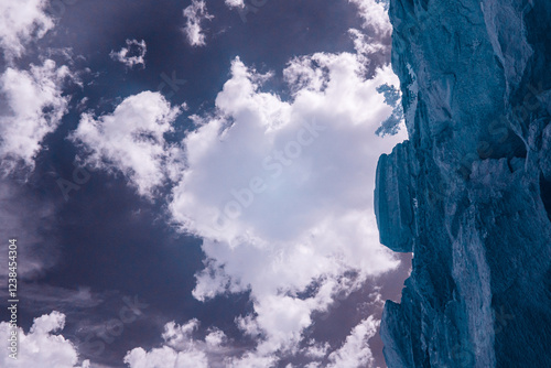 A dramatic, infrared-filtered image shows a steep, textured rock face rising against a partly cloudy sky, creating a contrasting yet harmonious scene. photo