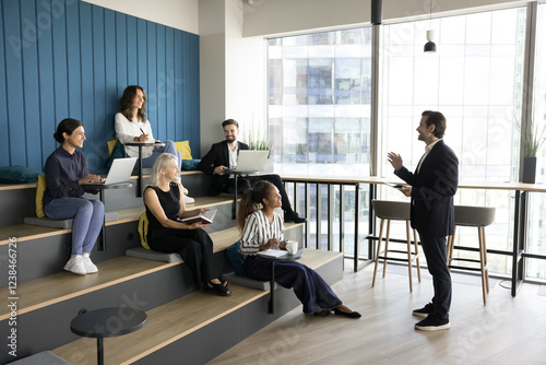 Diverse group of people engaged in training, lecture, briefing event or seminar seated on steps in auditorium, listen speech of teacher, leader or company boss, share ideas, knowledge and experience