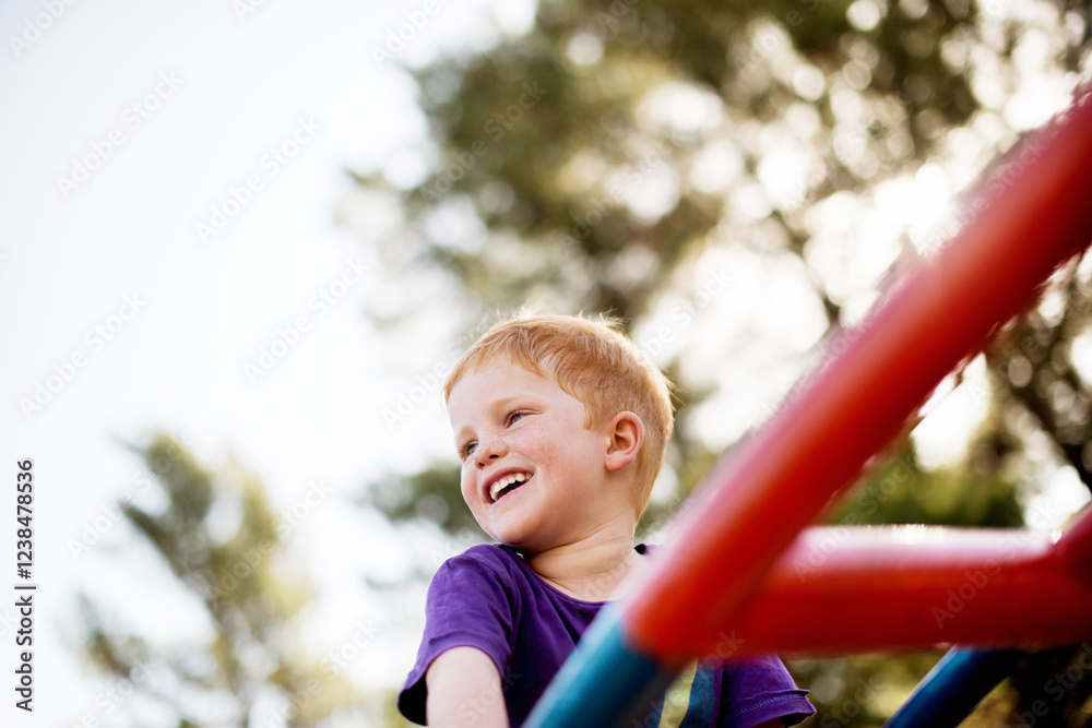 Excited, merry go round and smile with boy in forest for active play, child development or growth. Adventure, balance and game on carousel with happy kid having fun at playground in summer from below