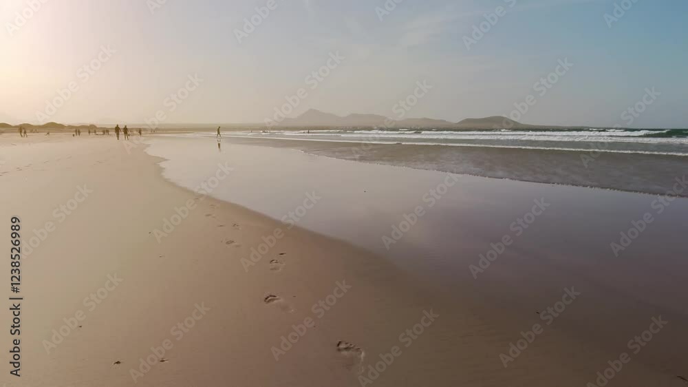 Sandstrand mit Menschen in der Abendsonne bei stimmungsvollem Sonnenuntergang, Meer, Caleta de Famarar, Urlaub, Idylle, Lanzarote, Kanaren, Küste, Landschaft, Bergsilhouetten, Surfer

