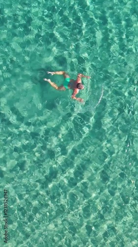 Woman swimming in emerald green waters of Sardinia Mediterranean sea. Summer relax and leisure. Top down aerial drone shot