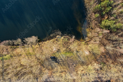 Parked car near lake shore in bare forest, aerial drone view