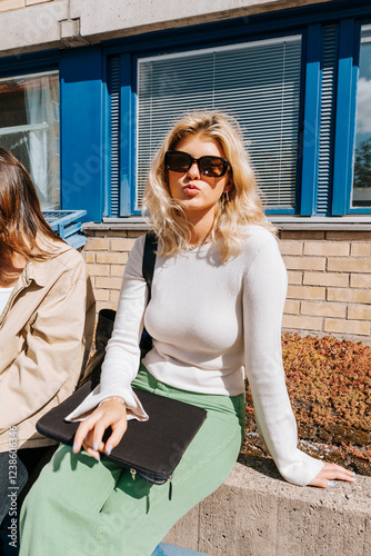 Young female student puckering lips while sitting on wall in college campus at sunny day photo