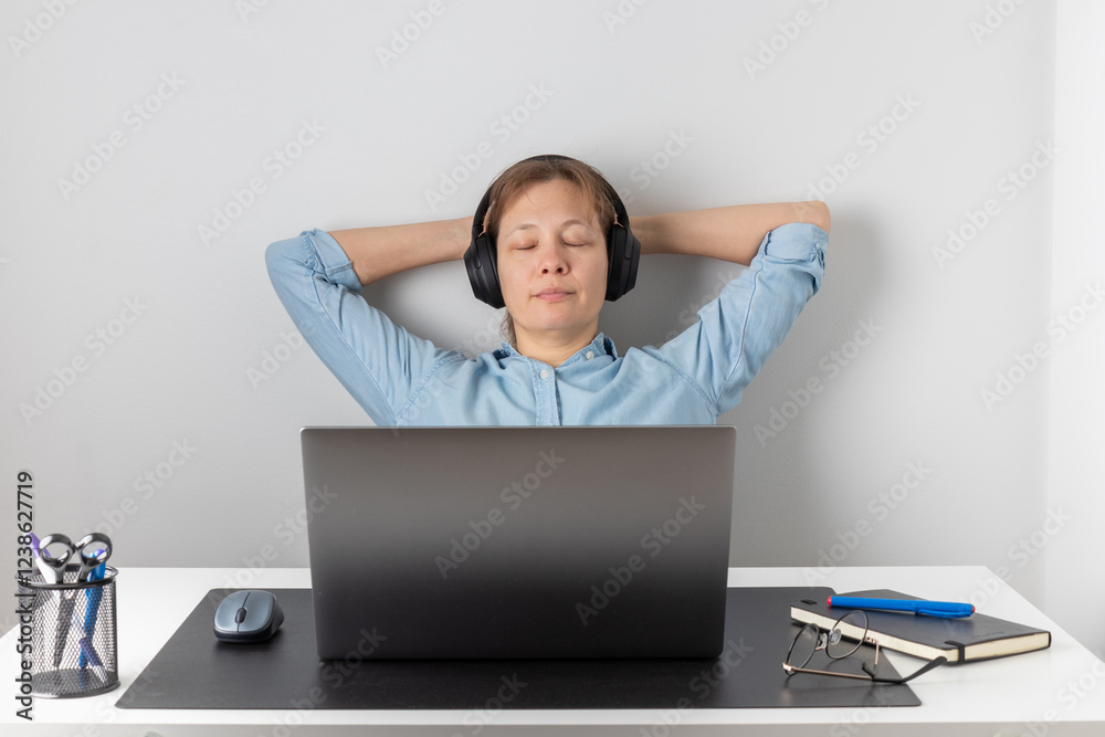 A calm nice freelancer woman putting on wireless headphones, sitting at the desk with laptop, listening with pleasure and relaxation her favorite music with her eyes closed A calm nice freelancer woman putting on wireless headphones, sitting at the desk with laptop, listening with pleasure and relaxation her favorite music with her eyes closed
