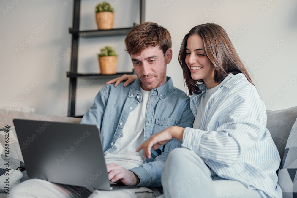 Happy millennial couple sit relax on couch in living room watching video on laptop together, smiling young husband and wife rest on sofa at home browsing Internet using modern computer device. Happy millennial couple sit relax on couch in living room watching video on laptop together, smiling young husband and wife rest on sofa at home browsing Internet using modern computer device.