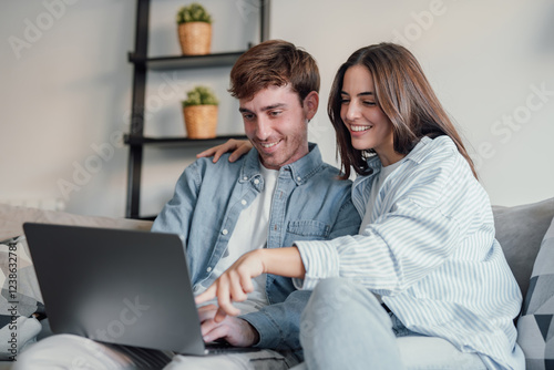 Tapeta Happy millennial couple sit relax on couch in living room watching video on laptop together, smiling young husband and wife rest on sofa at home browsing Internet using modern computer device