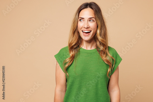 Young shocked surprised excited amazed happy woman she wear green t-shirt casual clothes look aside on area mock up isolated on plain pastel light beige background studio portrait. Lifestyle concept.