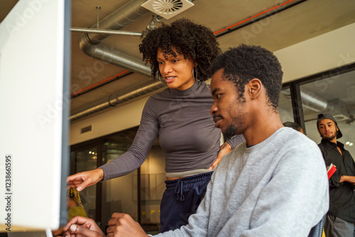 Low angle view of young coding professional talking with male colleague working on desktop PC in office photo