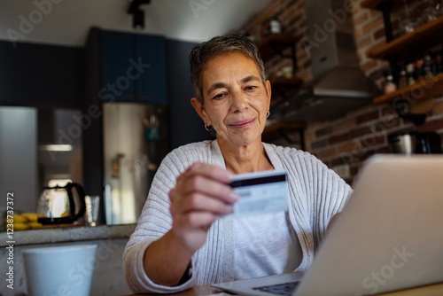 Smiling senior woman making a purchase on laptop with credit card at home photo