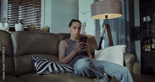 Принти на полотні A woman uses a mobile phone while sitting on the couch at home