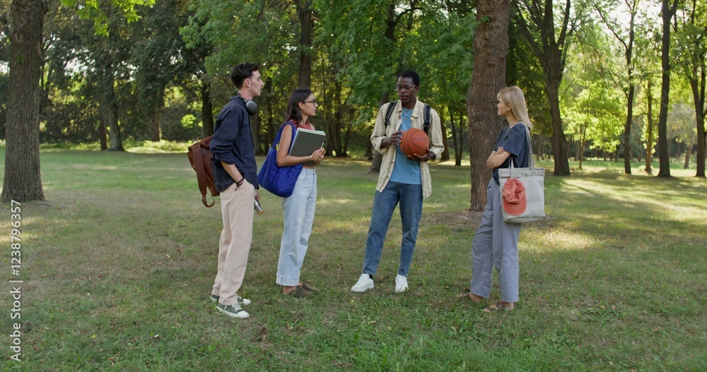 Obraz premium A group of young people with briefcases on their shoulders are talking standing in a city park. Students at recess