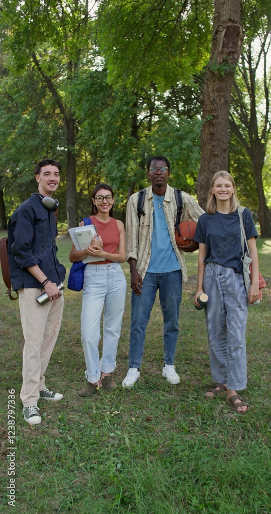 A group of young people with briefcases on their shoulders are smiling at the camera while standing in a city park. Summer day A group of young people with briefcases on their shoulders are smiling at the camera while standing in a city park. Summer day